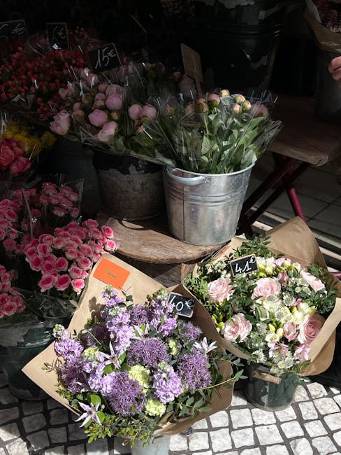 A display of fresh floral arrangements at a flower shop, featuring various bouquets with pink, purple, and white flowers. There are pink roses and carnations, purple statice and alliums, and white spr