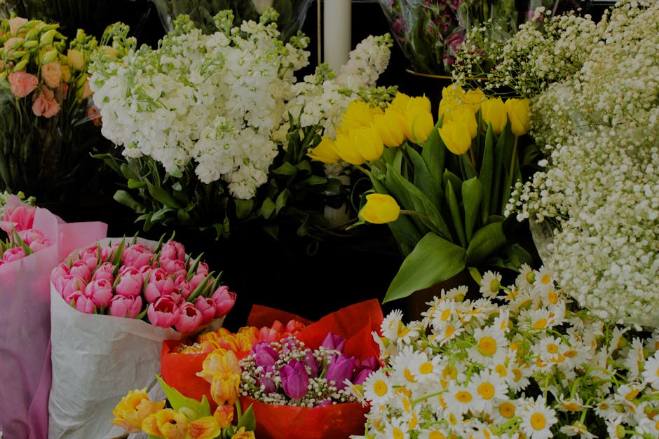 A vibrant floral arrangement featuring a variety of fresh flowers including bright yellow tulips with broad green leaves, delicate white daisies with yellow centers, clusters of small white baby's bre